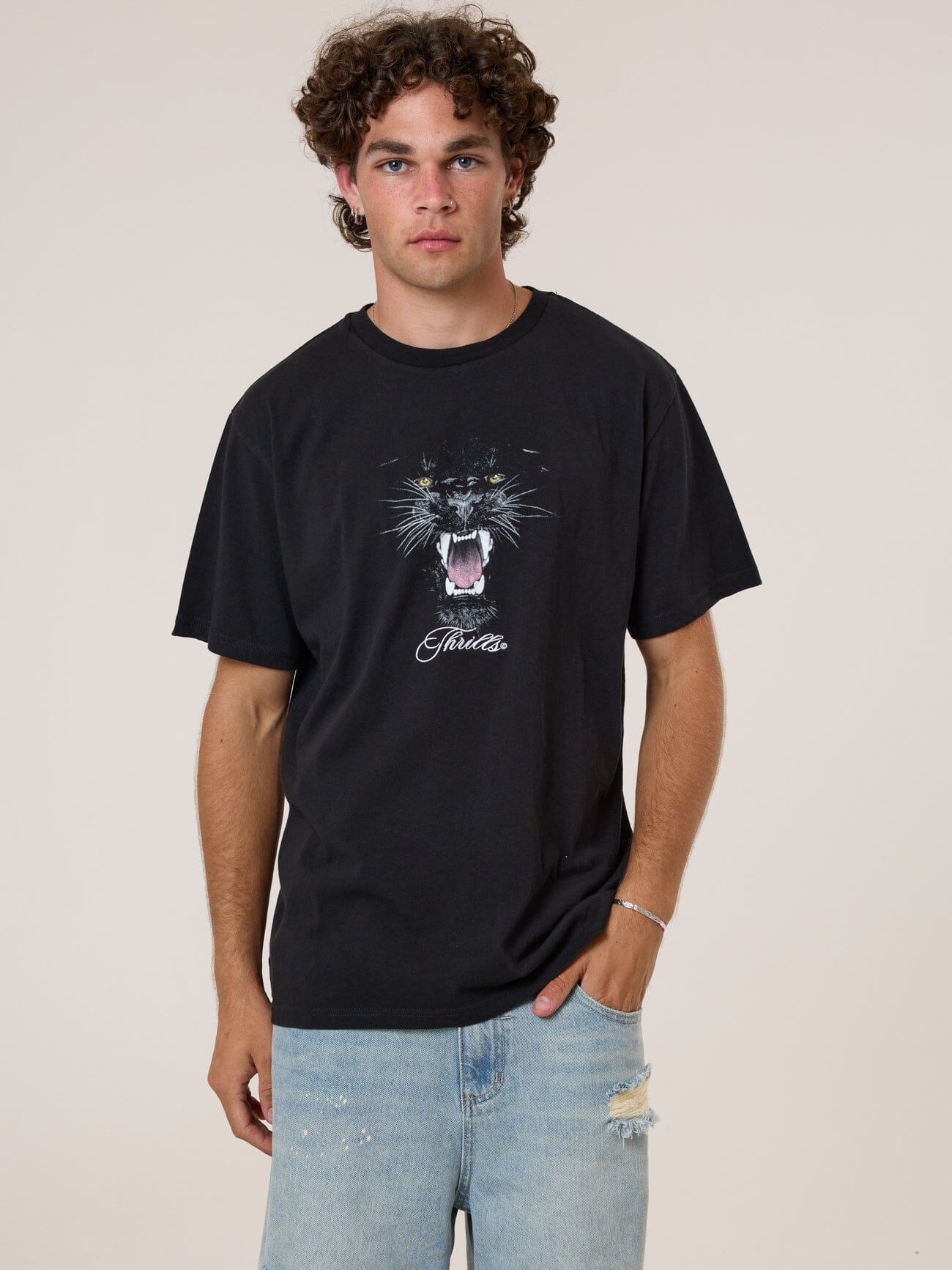 Male model wearing our Thrills Deadly Pursuit Merch Fit Tee in Black standing against a plain studio background.