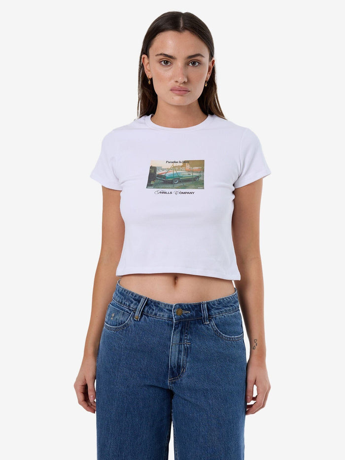 Female model wearing our Thrills Paradise Is Here Mini Tee in White standing against a plain studio background.