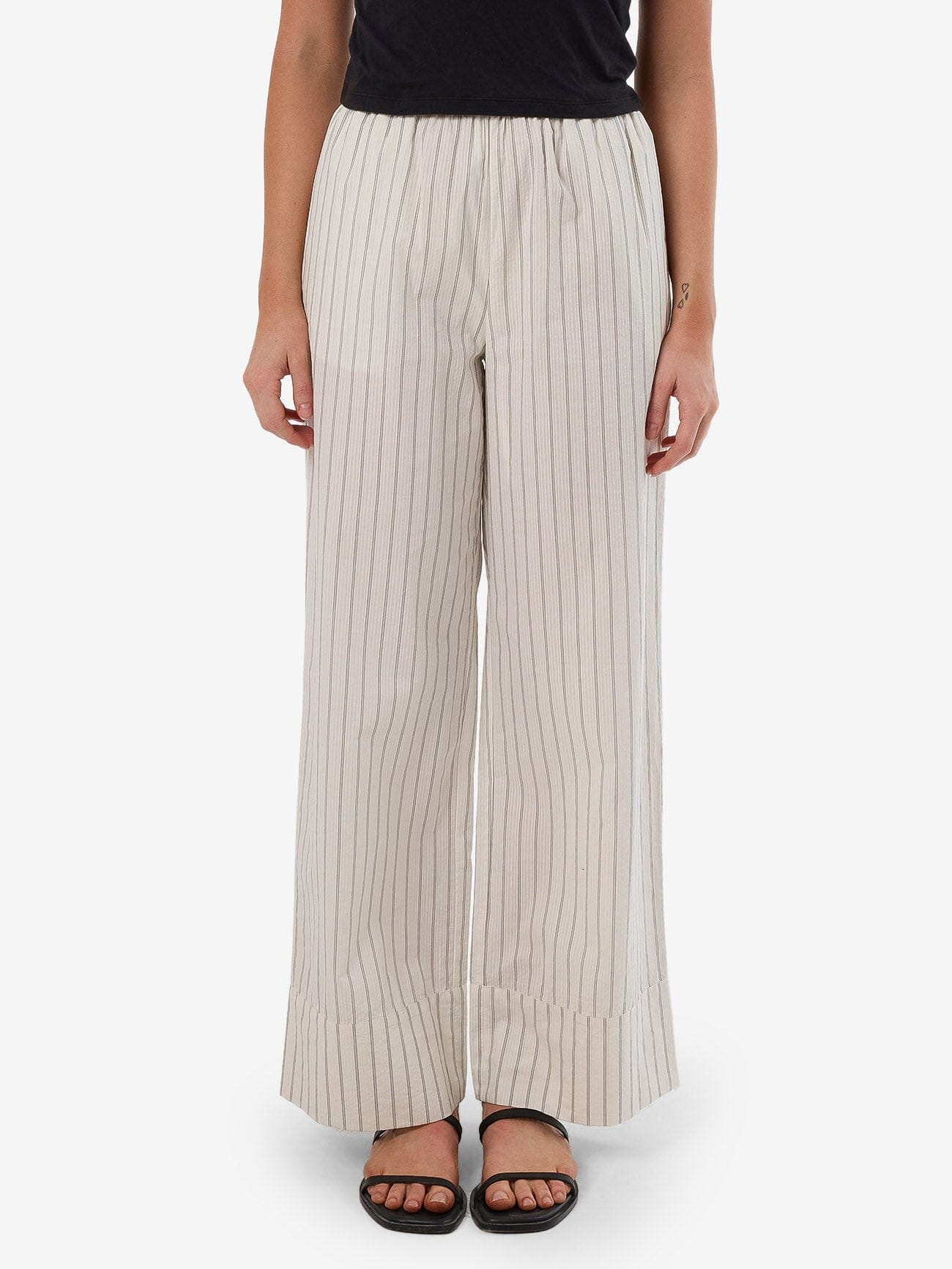 Female model wearing our Thrills Unwind Stripe Pant in White standing against a plain studio background.