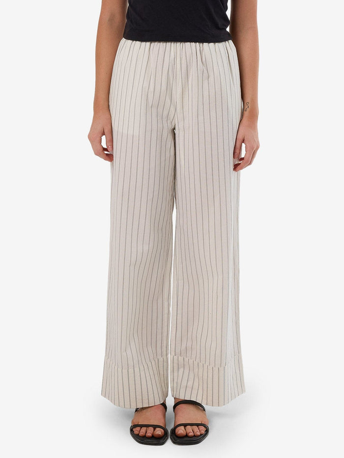 Female model wearing our Thrills Unwind Stripe Pant in White standing against a plain studio background.