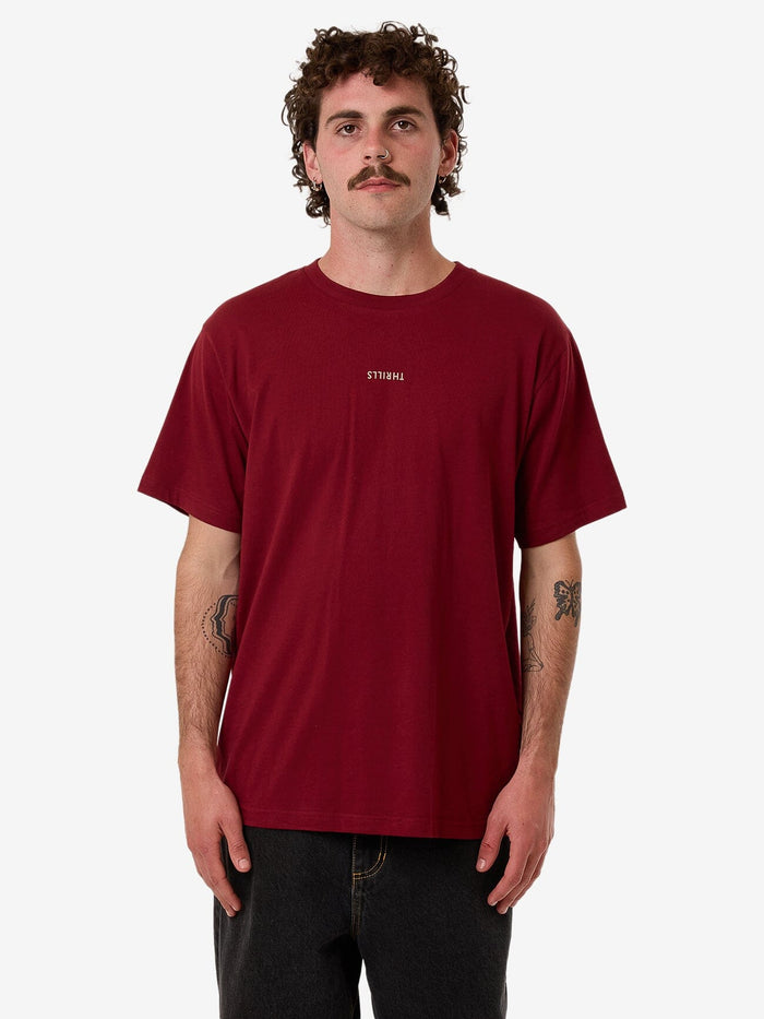 Male model wearing our Thrills Minimal Thrills Merch Fit Tee in Red standing against a plain studio background.