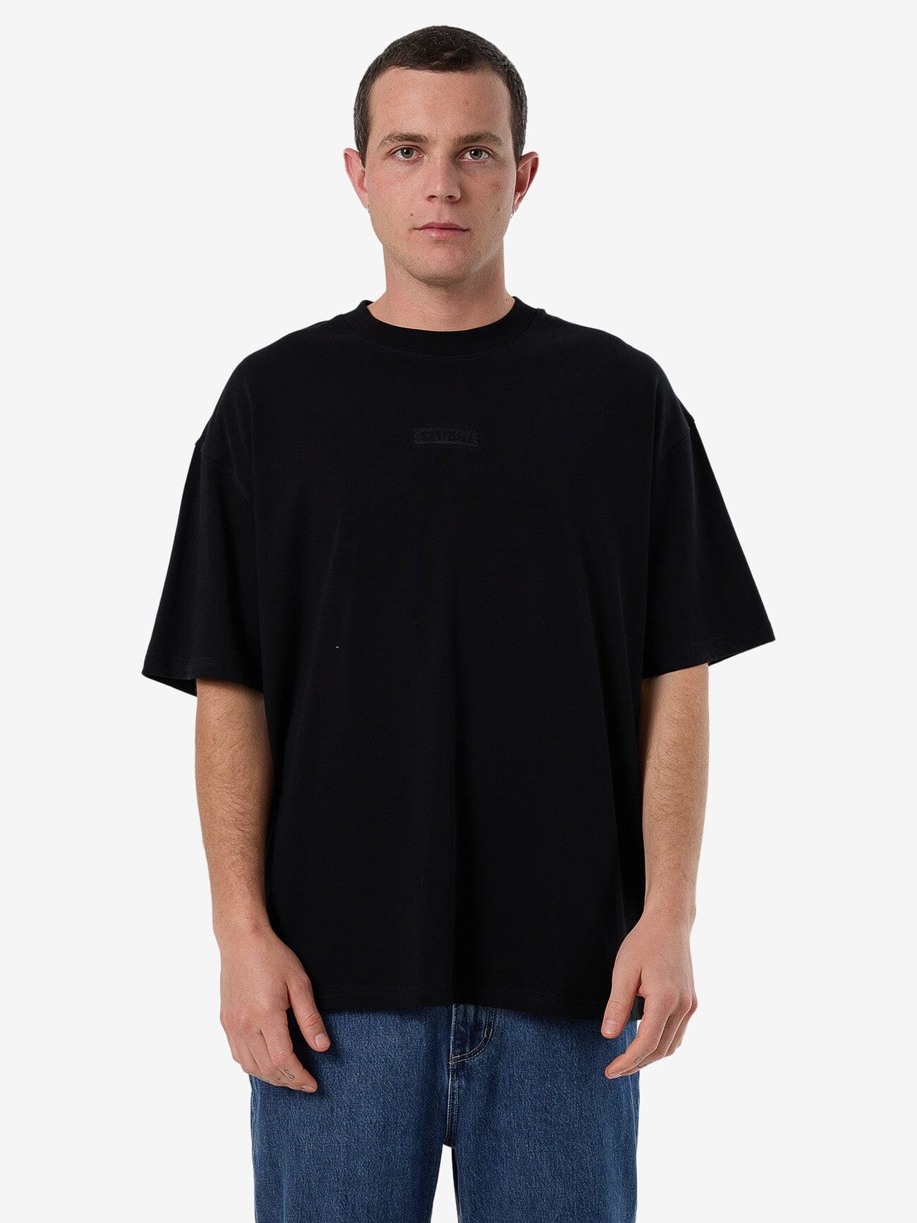 Male model wearing our Thrills Superior Thrills Box Fit Oversize Tee in Black standing against a plain studio background.