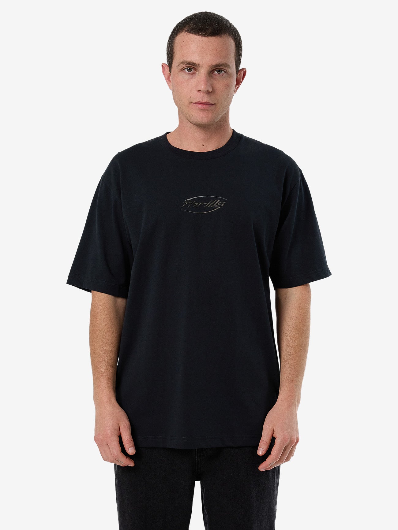 Male model wearing our Thrills Fortune Favors Embro Oversize Fit Tee in Black standing against a plain studio background.