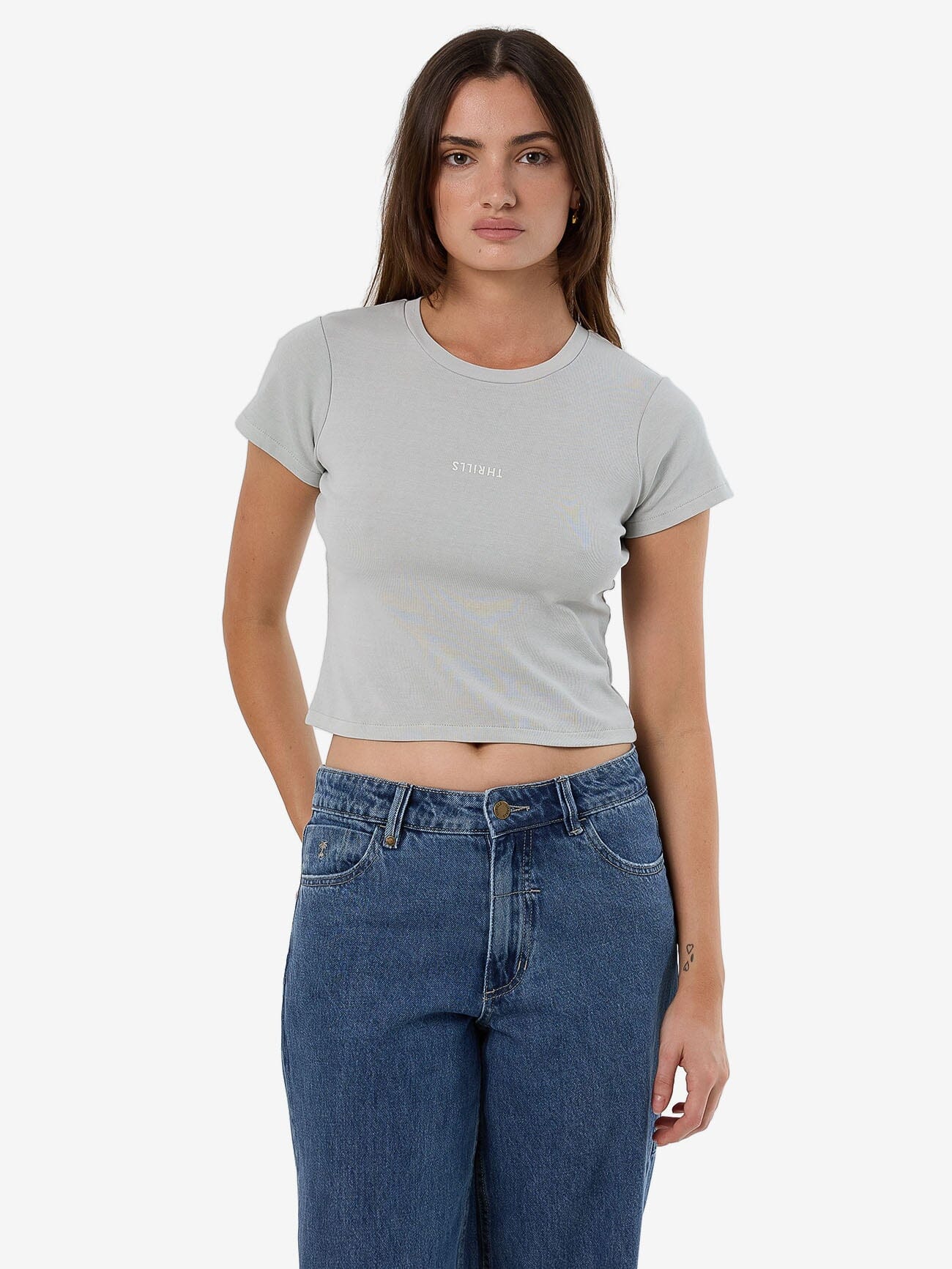 Female model wearing our Thrills Minimal Thrills Mini Tee in White standing against a plain studio background.