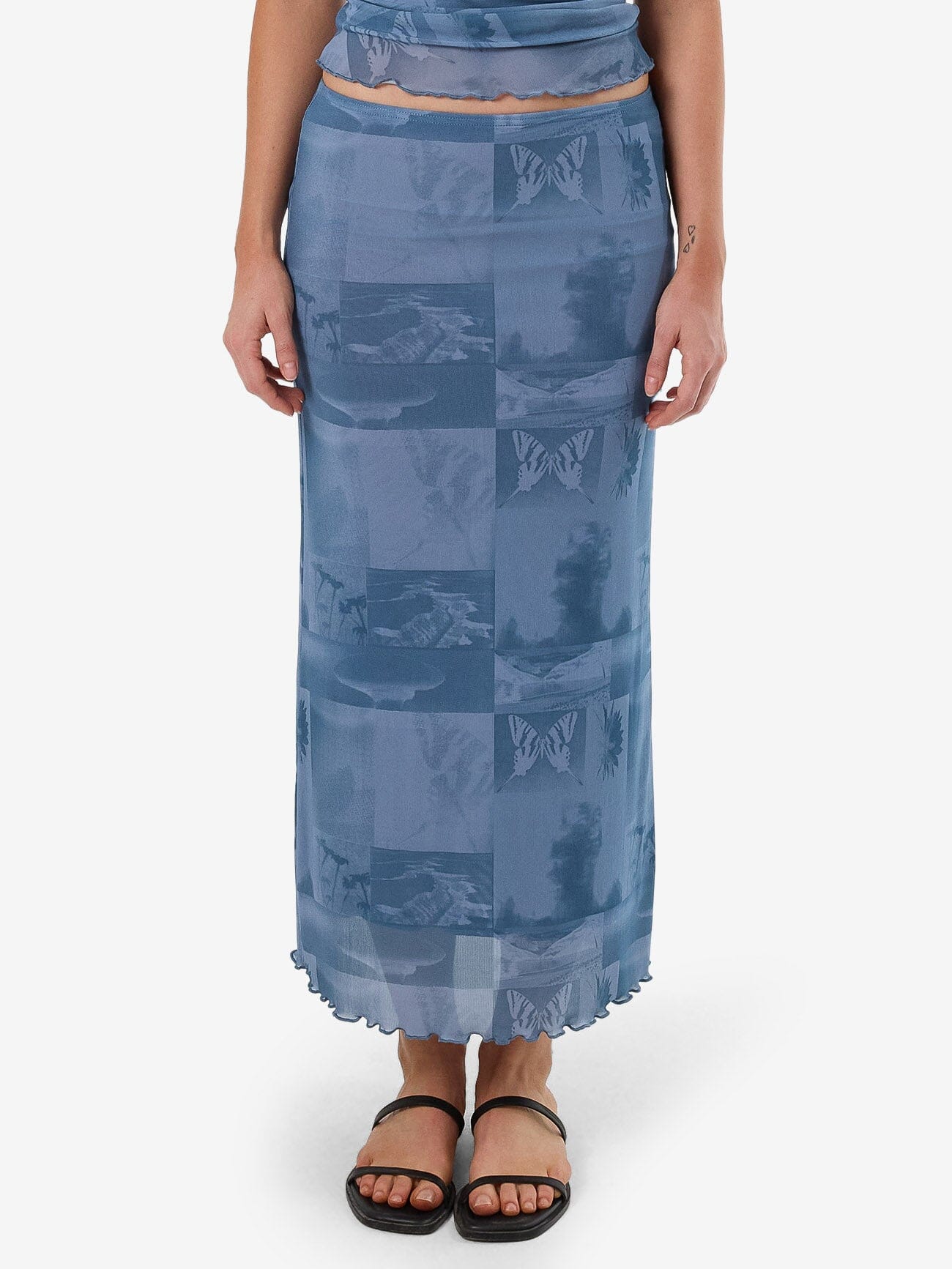 Female model wearing our Thrills Eclipse Haze Mesh Skirt in Blue standing against a plain studio background.