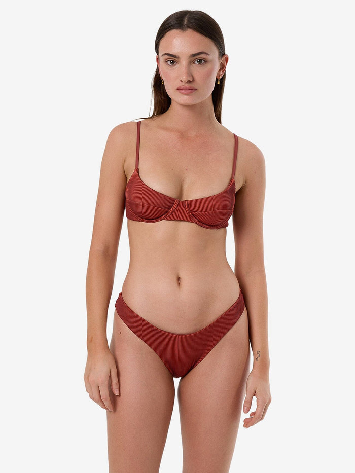 Female model wearing our Thrills Alba Rib Classic Bikini Bottom in Orange standing against a plain studio background.